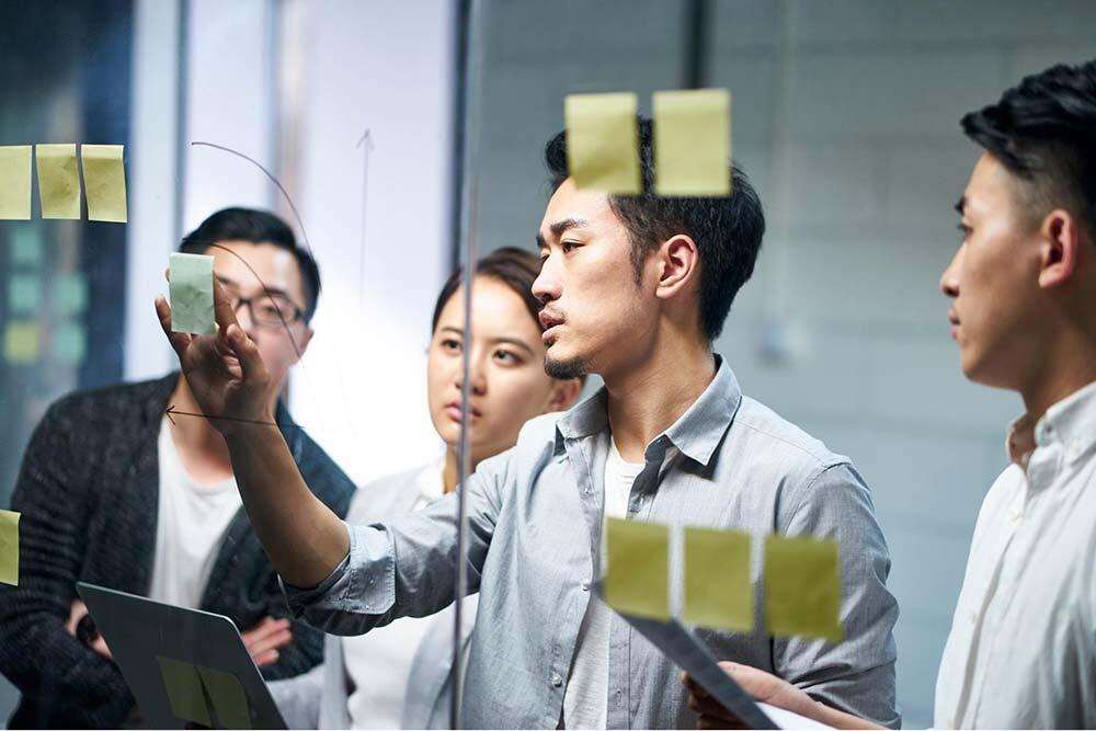 Businessman putting a adhesive note on glass in office during team meeting, formulating business strategies.