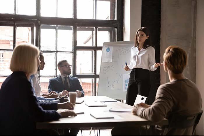 Businesswoman standing near flipchart with financial charts and talking to her colleagues