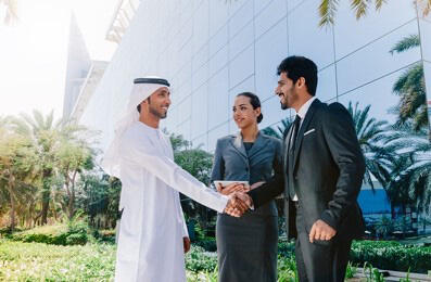 Two business professionals shaking hands in front of a modern office building.