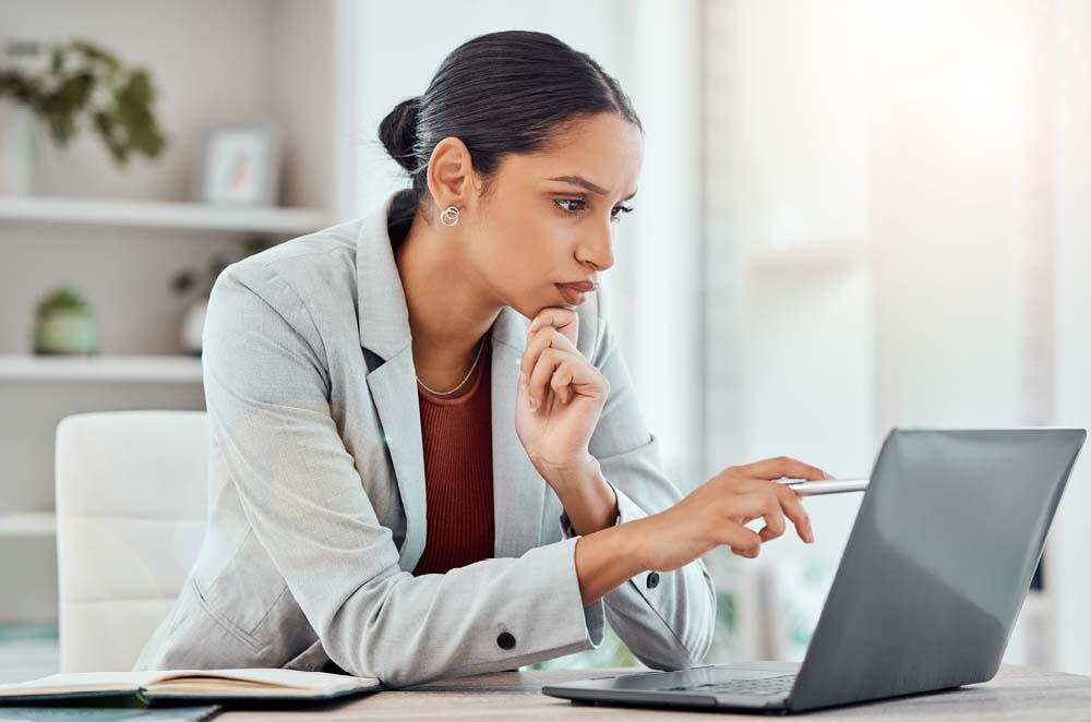 A woman in a business suit intently examines her laptop screen in a professional setting.