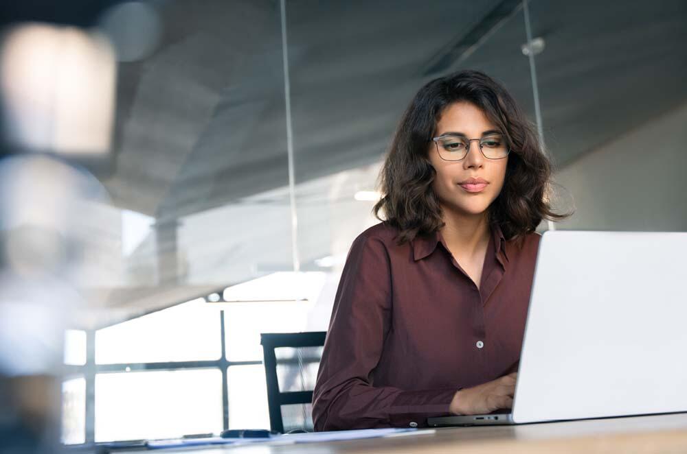 A woman wearing glasses is focused on her work while typing on a laptop.